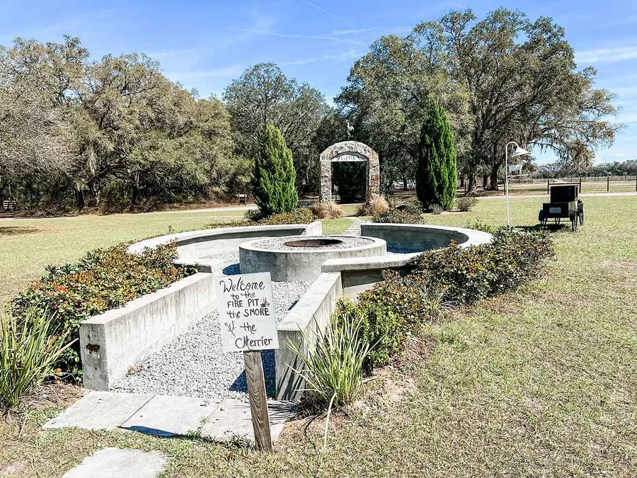 The stone fire pit and garden arch under oak trees on a sunny morning