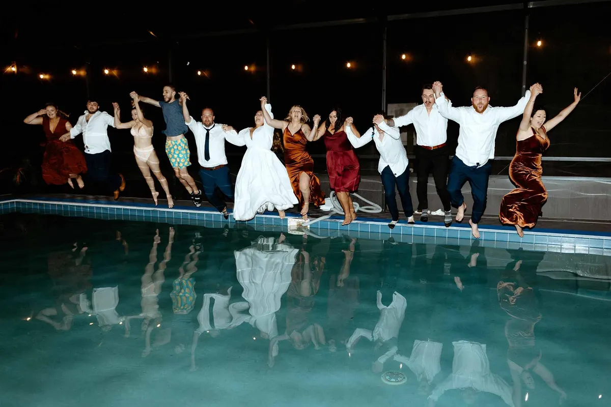 A wedding party jumping into the pool at night