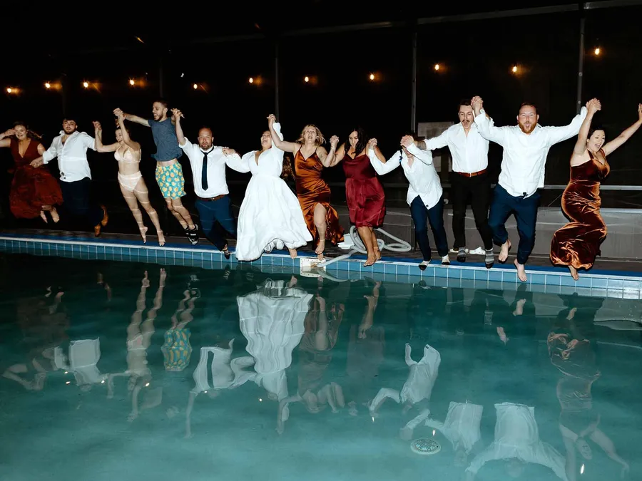 A wedding party jumping into the pool at night